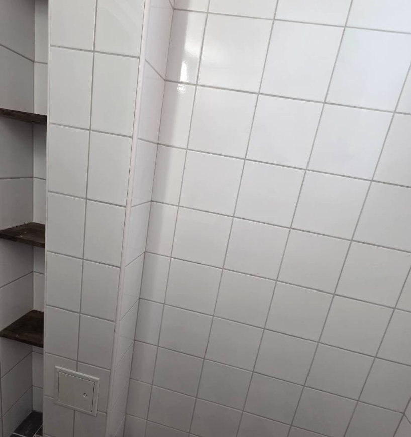 Vit kaklad vägg med inbyggd nisch och trähyllor för förvaring.